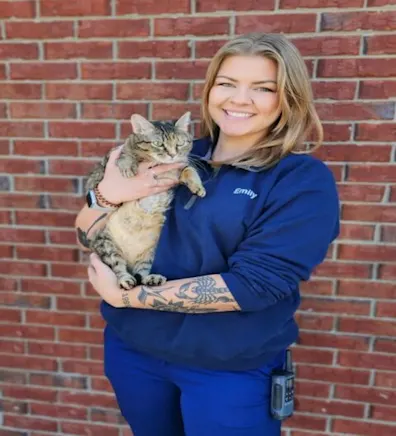 Emily holding onto a tabby cat while smiling in front of a brick wall. Emily holding onto a tabby cat while smiling in front of a brick wall.