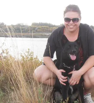 Angela Oranchuk in front of a lake with a black dog Angela Oranchuk in front of a lake with a black dog