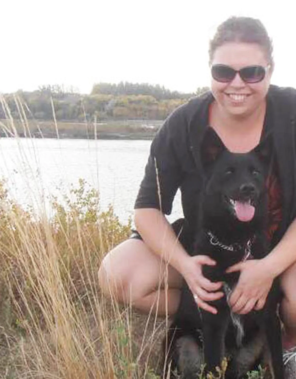 Angela Oranchuk in front of a lake with a black dog Angela Oranchuk in front of a lake with a black dog
