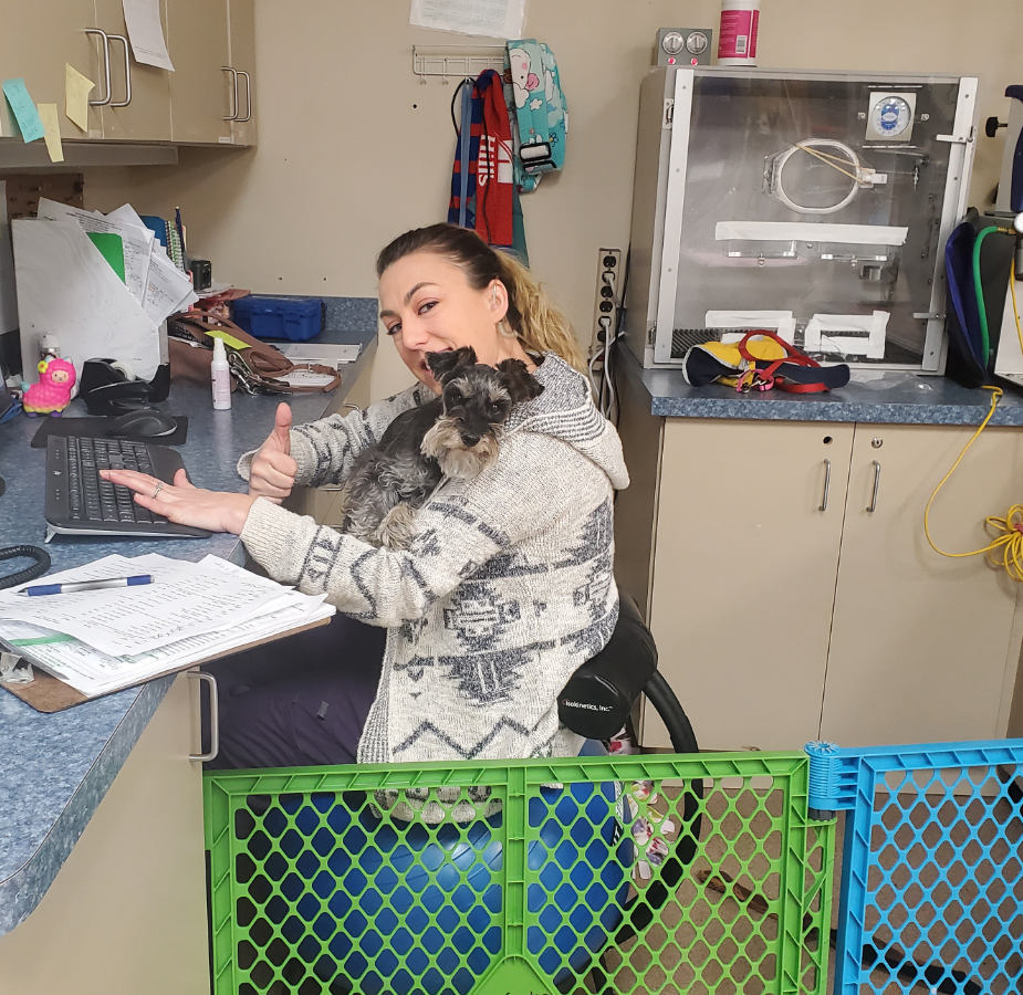 Staff member sitting at a desk with her thumb up and a dog in her lap