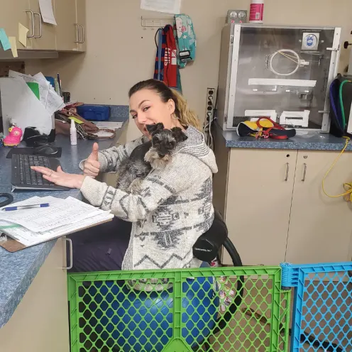 Staff member sitting at a desk with her thumb up and a dog in her lap
