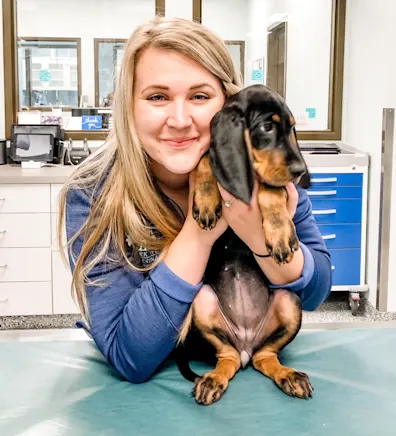 Allie Causey smiling holding up a Bloodhound puppy on an exam table Allie Causey smiling holding up a Bloodhound puppy on an exam table