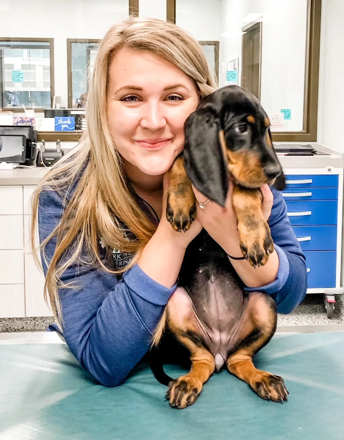 Allie Causey smiling holding up a Bloodhound puppy on an exam table Allie Causey smiling holding up a Bloodhound puppy on an exam table