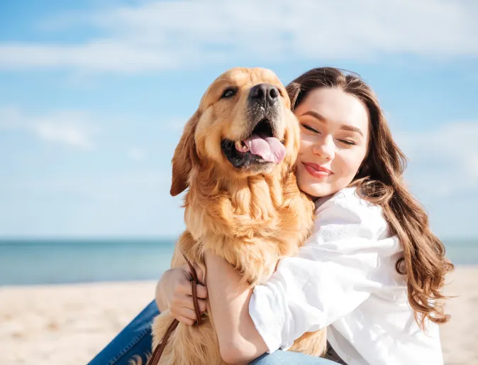 Dog and woman sitting on the beach hugging. 