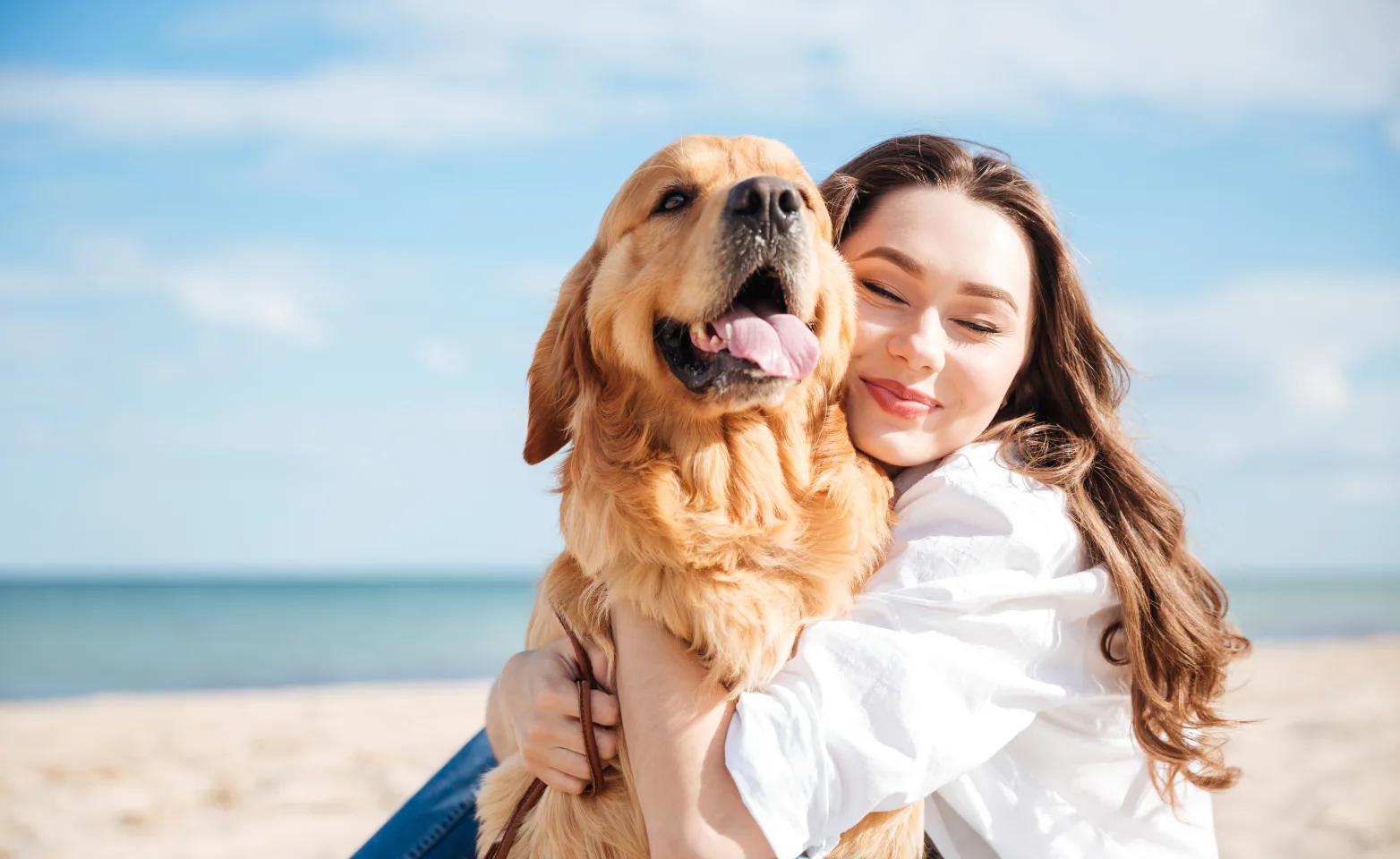 Dog and woman sitting on the beach hugging. 