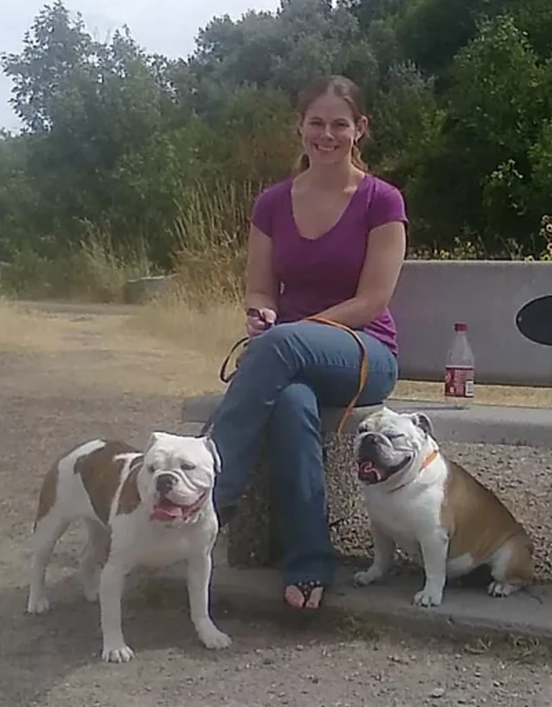 Rebecca R. sitting on a bench with two dogs next to her Rebecca R. sitting on a bench with two dogs next to her