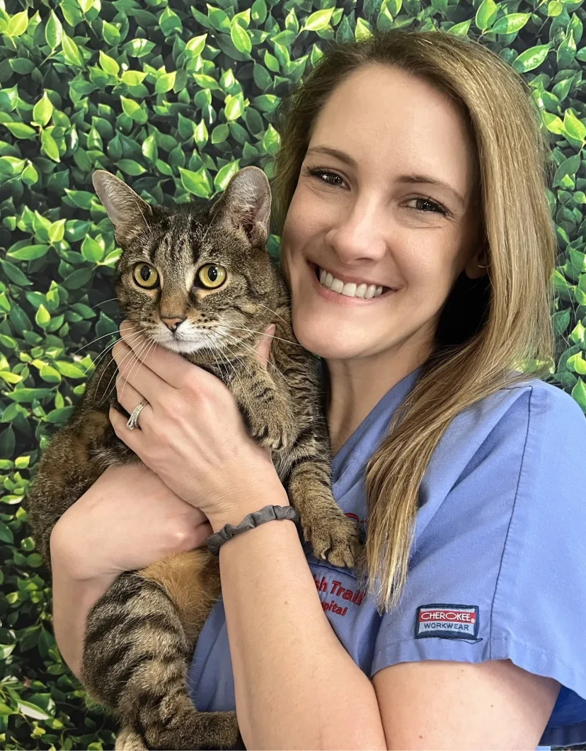 Lindsay C.'s staff photo from Spanish Trail Animal Hospital where she is outside in the front yard holding a fluffy brown dog in her arms.