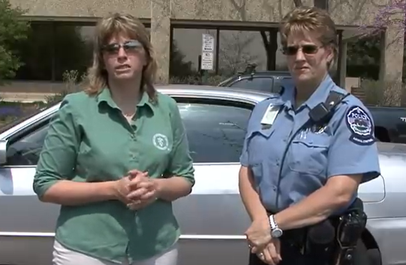 Woman with a green shirt speaking to camera with police officer next to her