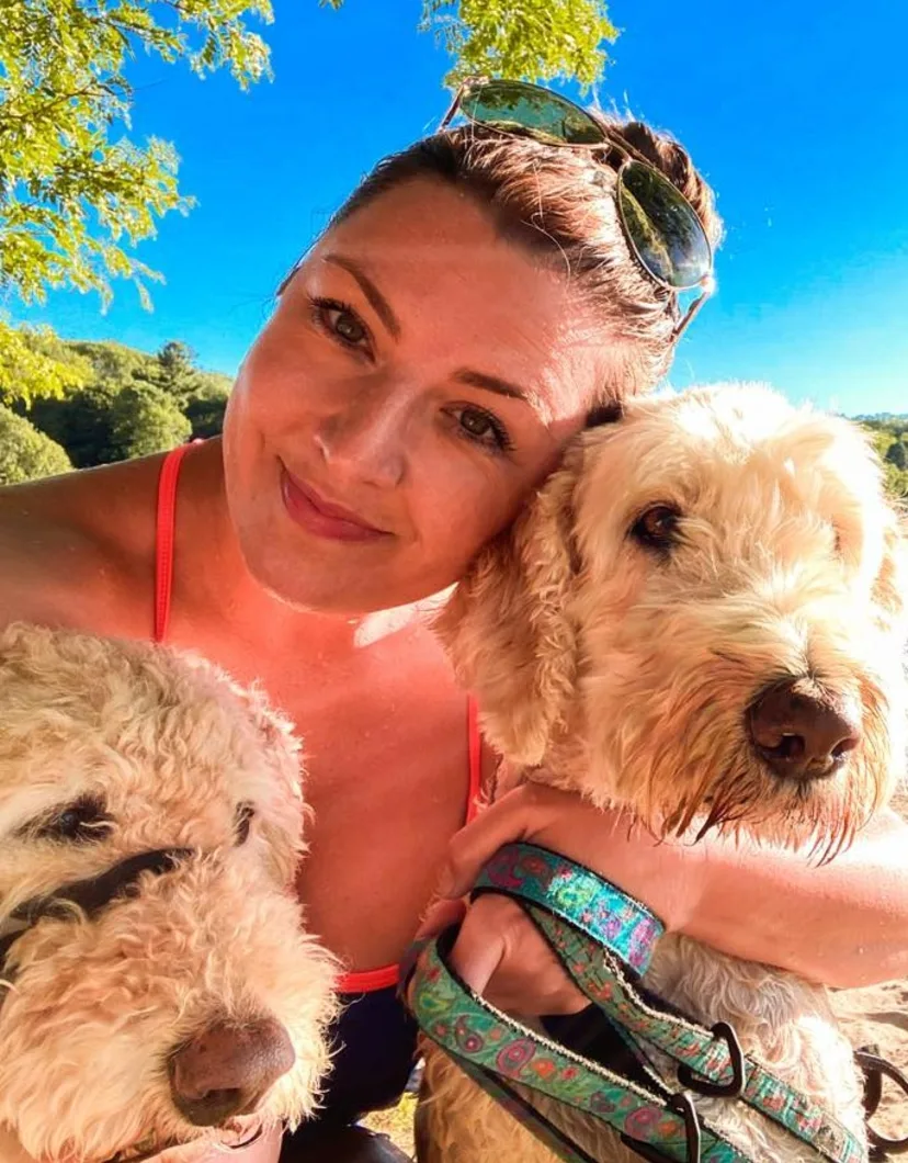 Dr. Natalie Reid cuddling with two beige dogs on a beach