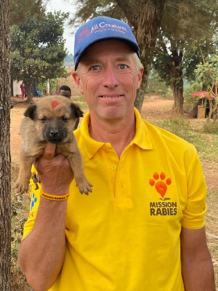 Dr. Joe smiling standing outside holding a small brown puppy