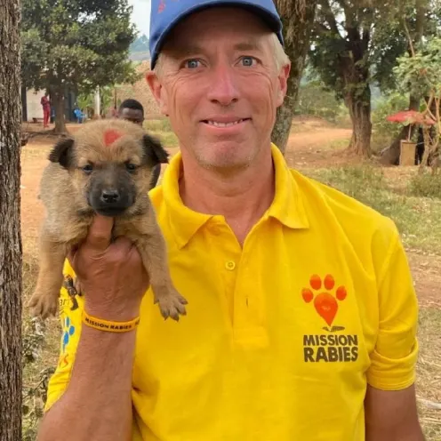 Dr. Joe smiling standing outside holding a small brown puppy