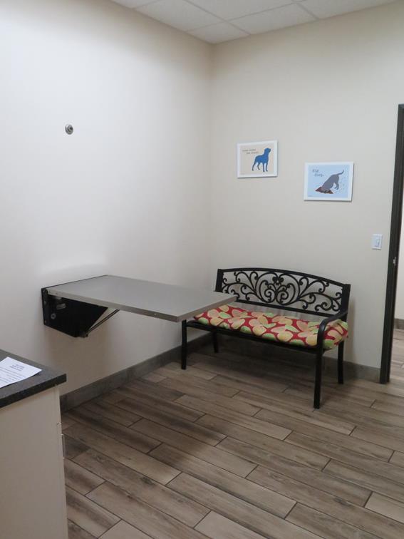 An exam room with an exam table stuck to the wall and a bench in the examination room. 