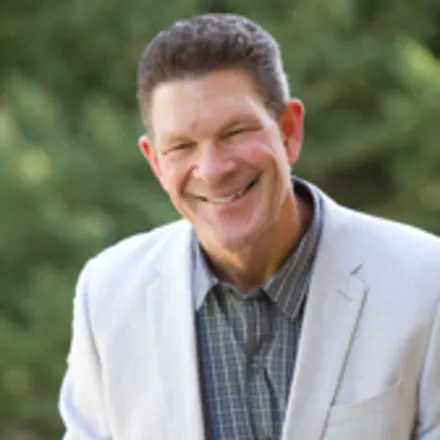 Dr. Terry Silkman wearing white lab coat over dress shirt in front of a green outdoor backdrop