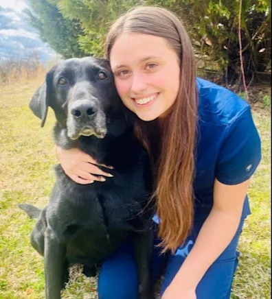 Madalyn holding onto a black labrador in a grassy field while smiling for a photo. Madalyn holding onto a black labrador in a grassy field while smiling for a photo.