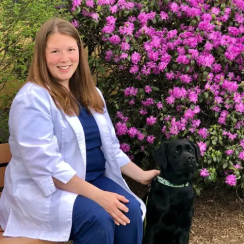 Dr. Kate DeLisle of Northampton Veterinary Clinic sitting on a bench outside while petting a dog Dr. Kate DeLisle of Northampton Veterinary Clinic sitting on a bench outside while petting a dog