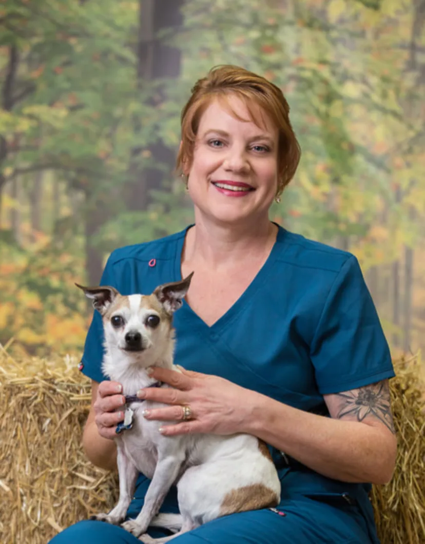 Linda dressed in blue scrubs holding a small tan and white dog