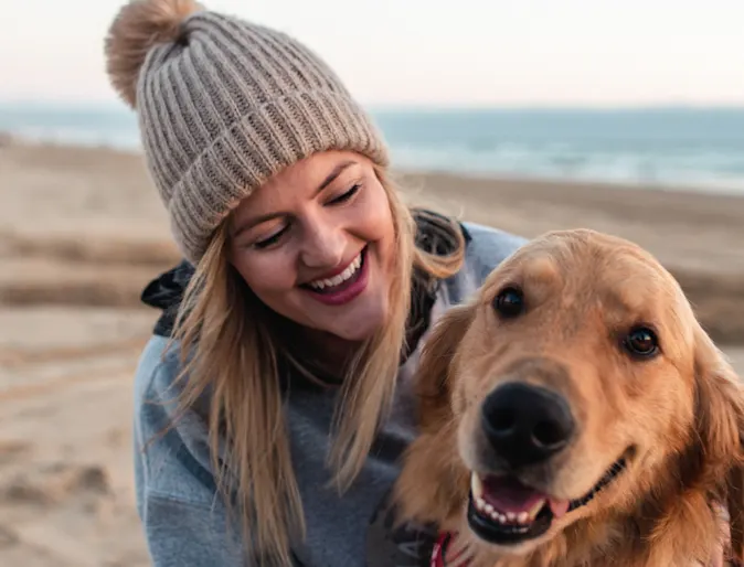 Woman hugging dog on the sand. Both are smiling