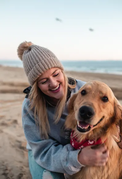 Woman hugging dog on the sand. Both are smiling