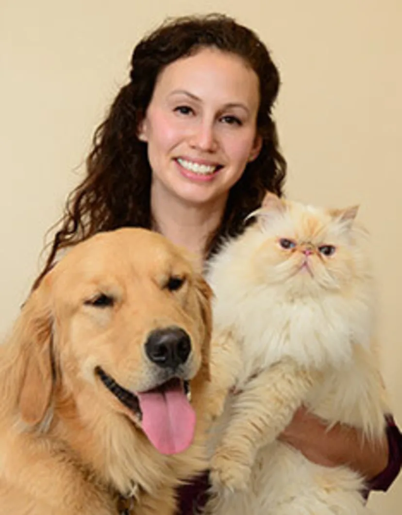 Dr. Ruthie Fliflet's staff photo from Anne Arundel Veterinary Emergency Clinic where she is sitting next to her adult golden retriever and holding her white fluffy cat in one arm.