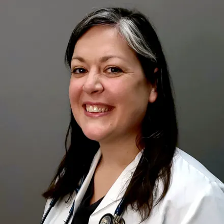 Diana Capozzi smiling standing in front of a grey wall wearing a white lab coat