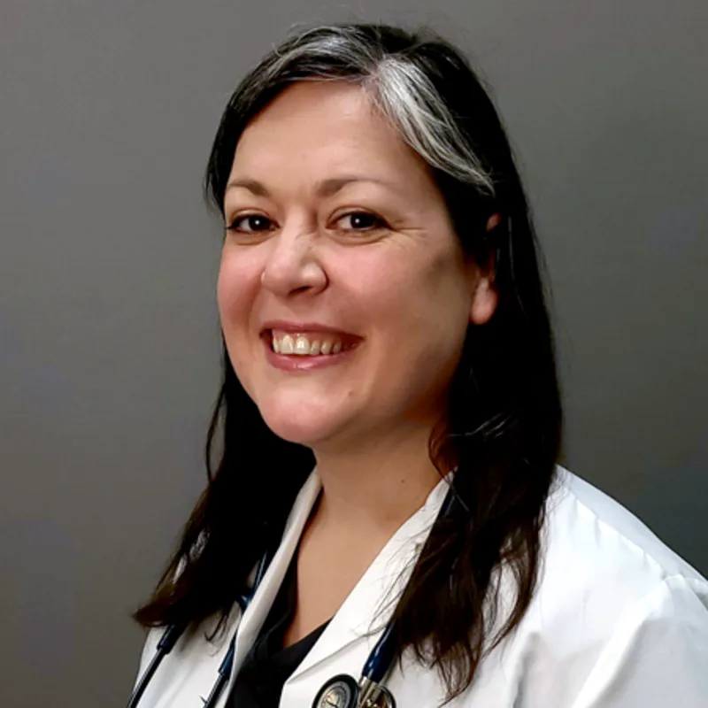 Diana Capozzi smiling standing in front of a grey wall wearing a white lab coat Diana Capozzi smiling standing in front of a grey wall wearing a white lab coat