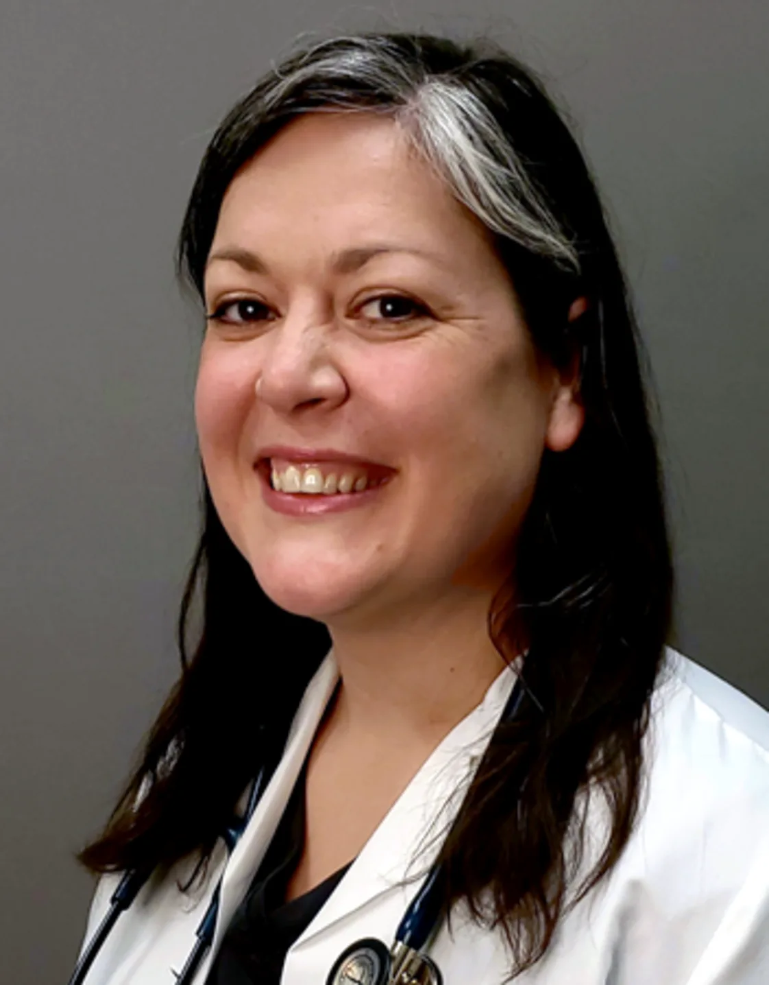 Diana Capozzi smiling standing in front of a grey wall wearing a white lab coat Diana Capozzi smiling standing in front of a grey wall wearing a white lab coat
