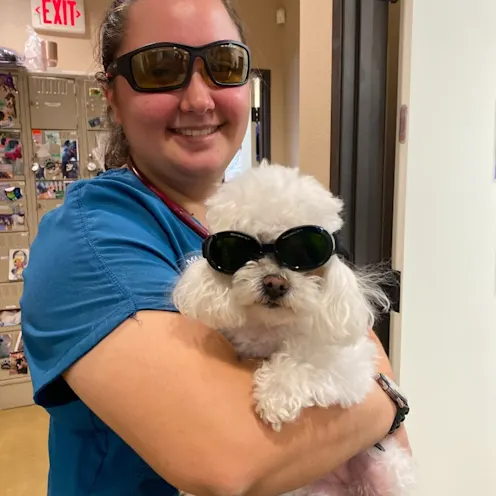 Woman in blue scrubs holding white fluffy dog while they both wear sunglasses. Woman in blue scrubs holding white fluffy dog while they both wear sunglasses.