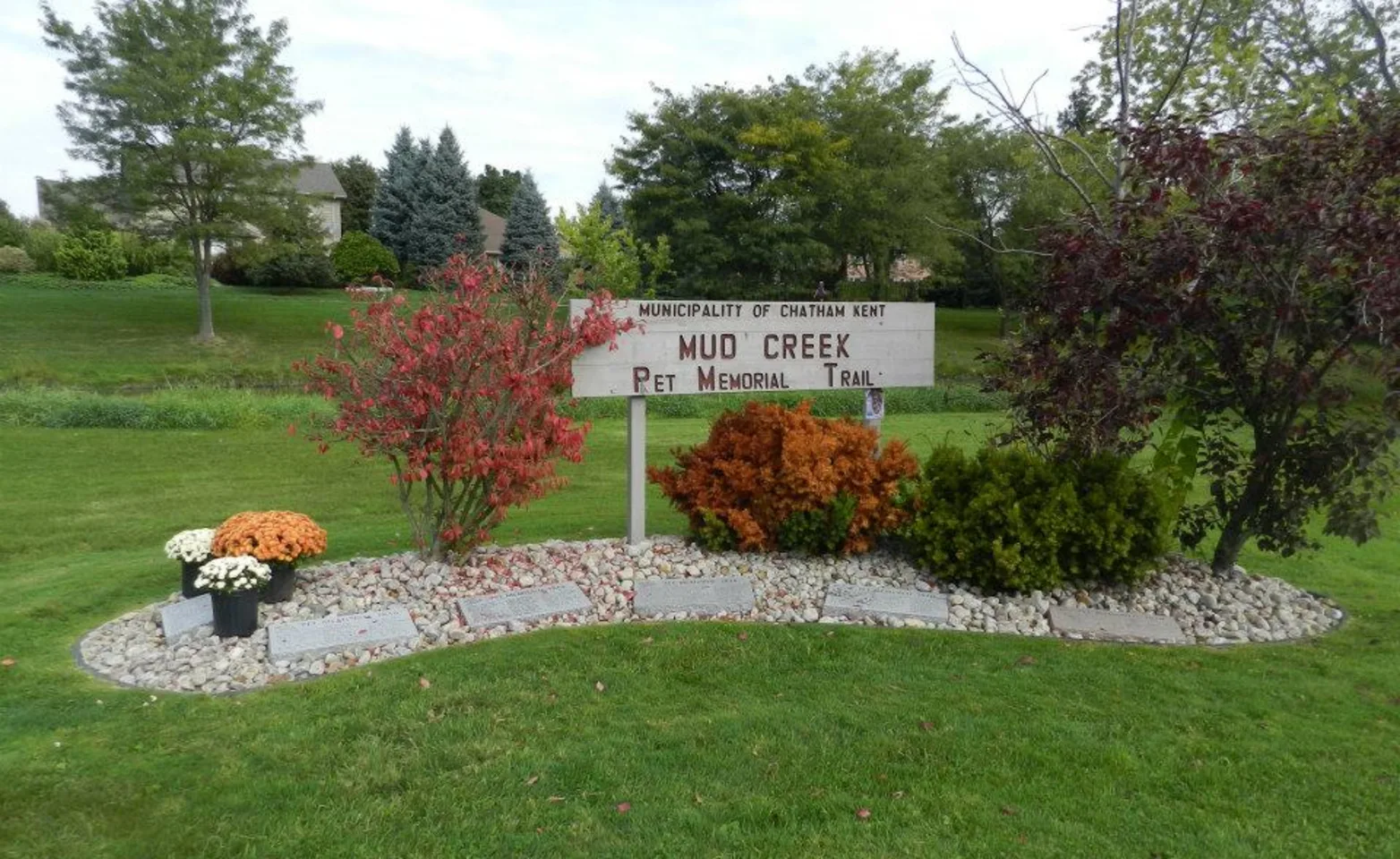 Mud Creek Memorial Trail sign in park with flowers Mud Creek Memorial Trail sign in park with flowers