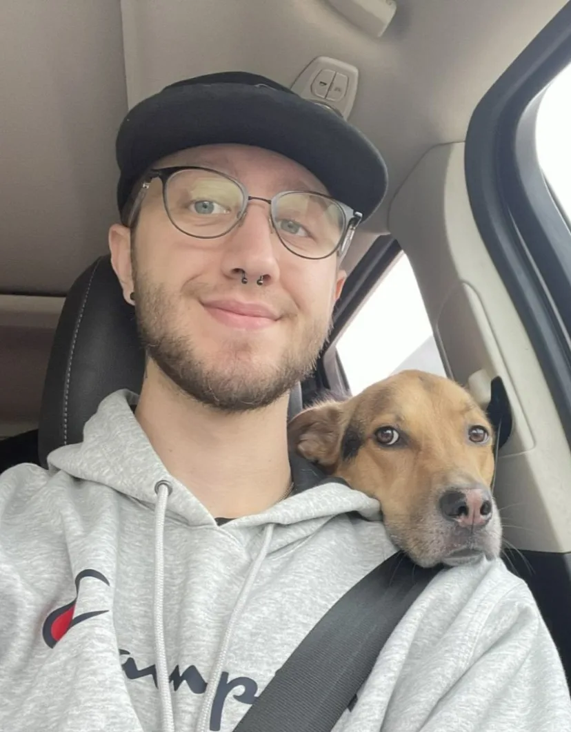 Trent in a car with his dog laying their head on his shoulder