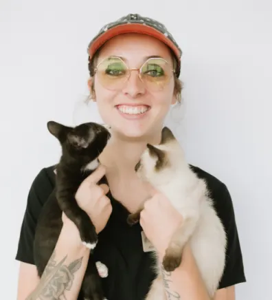 A portrait photo of Kennel Assistant Lauren holding a fluffy dog that is licking their face