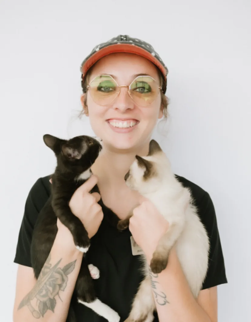 A portrait photo of Kennel Assistant Lauren holding a fluffy dog that is licking their face