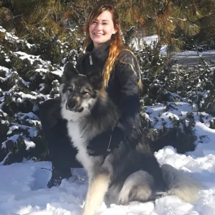 Dr. Anna Huber kneeling in snow with a fluffy dog