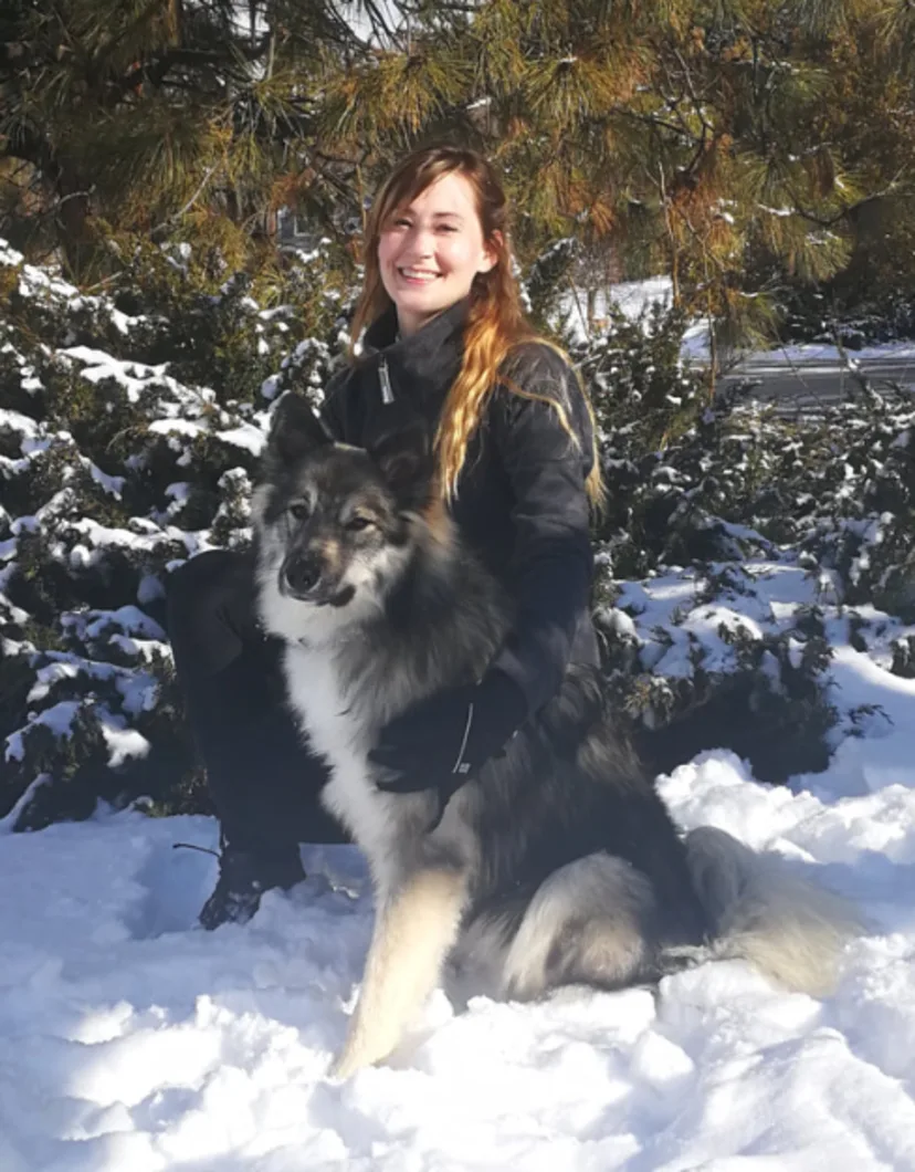 Dr. Anna Huber kneeling in snow with a fluffy dog
