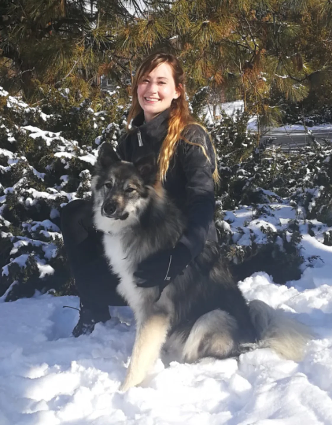 Dr. Anna Huber kneeling in snow with a fluffy dog Dr. Anna Huber kneeling in snow with a fluffy dog