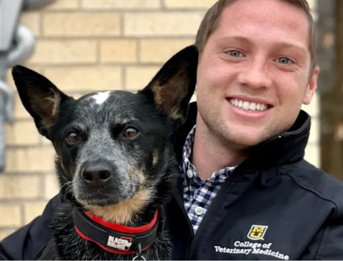 Male extern veterinarian holding a black dog Male extern veterinarian holding a black dog