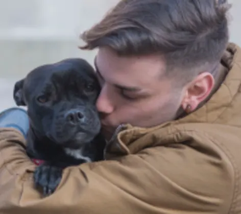 Gentleman is sitting on the ground hugging and kissing his black puppy lovingly.