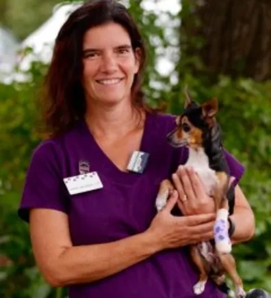 Chris standing in front of greenery while holding a dog Chris standing in front of greenery while holding a dog