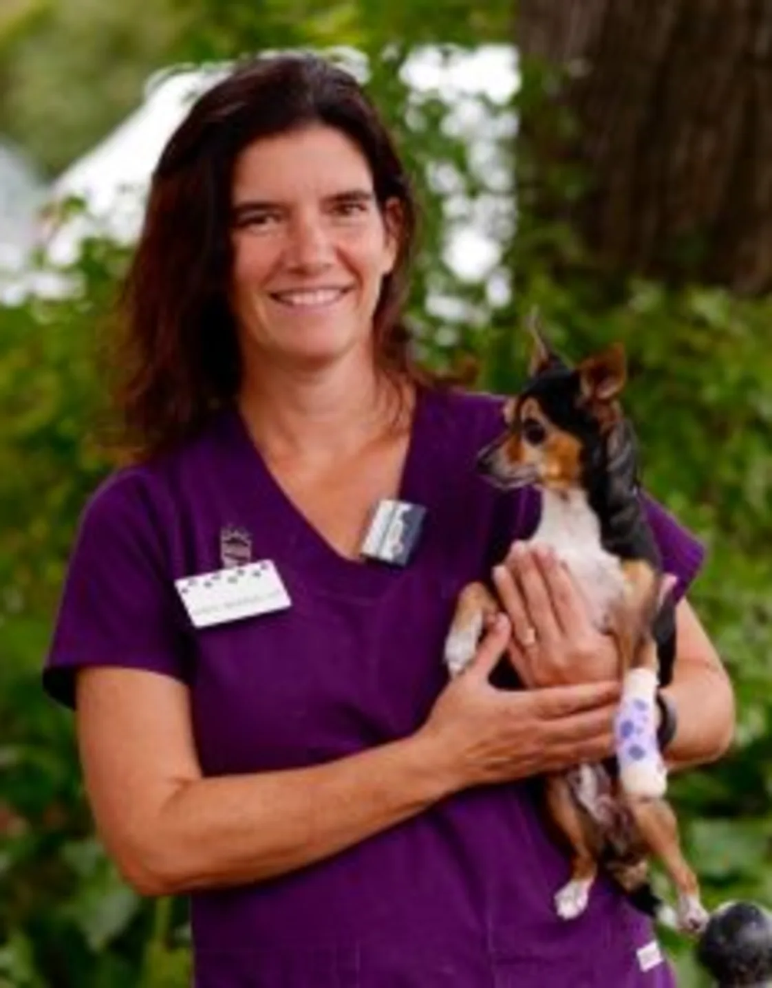 Chris standing in front of greenery while holding a dog Chris standing in front of greenery while holding a dog