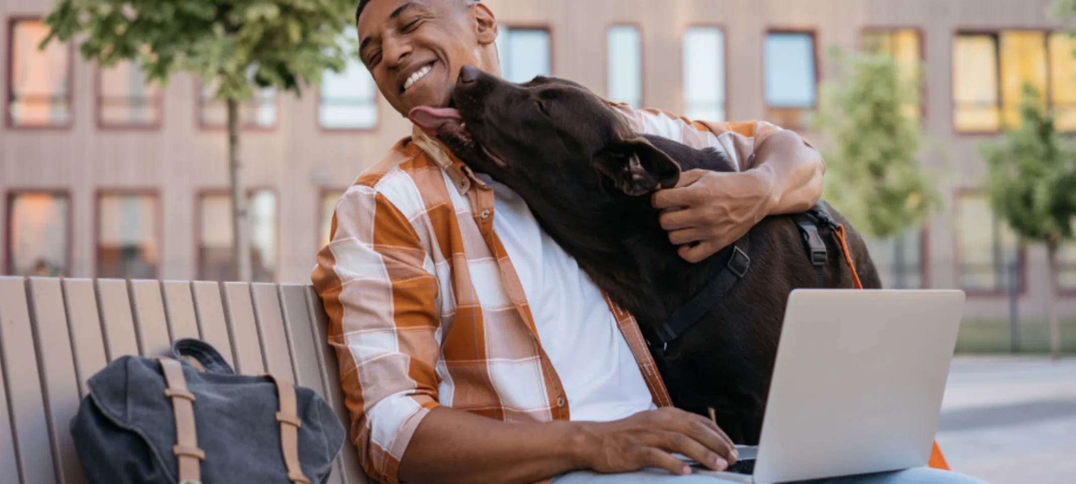 Dog Kissing Man using his Laptop Outside