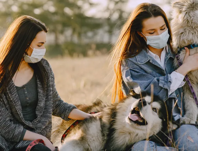 2 girls with mask on with their two dogs outside in a field