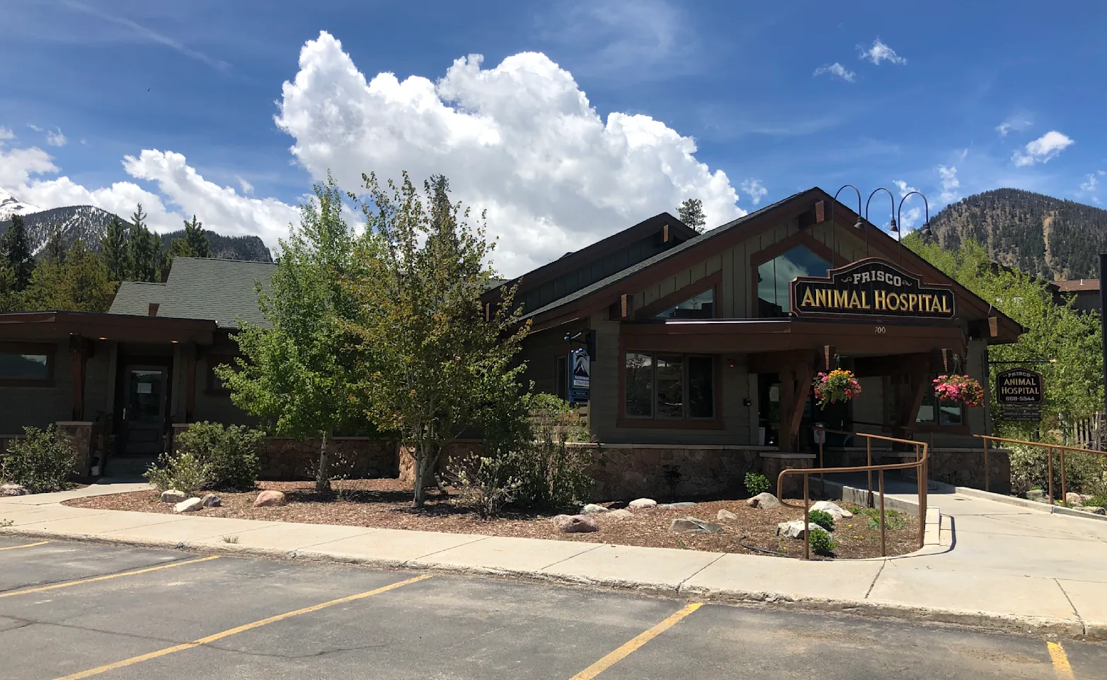 Front entrance and parking area of Frisco Animal Hospital with backdrop of blue skies, clouds, and mountains