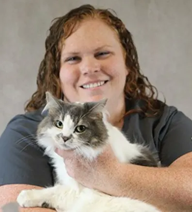 Amy Snyder smiling in front of a grey backdrop holding a white and grey cat