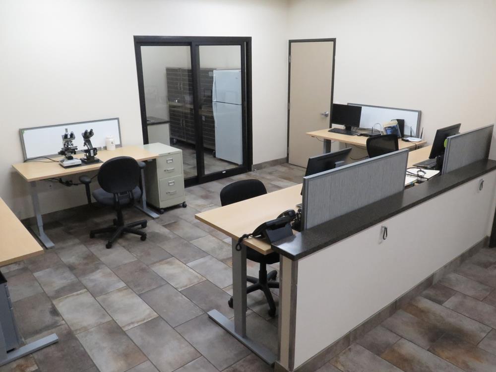 A lab showing desks filled with computers and chairs along with microscope on a desk. 
