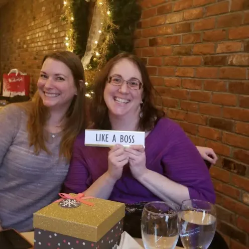 Two staff members smiling with little sign