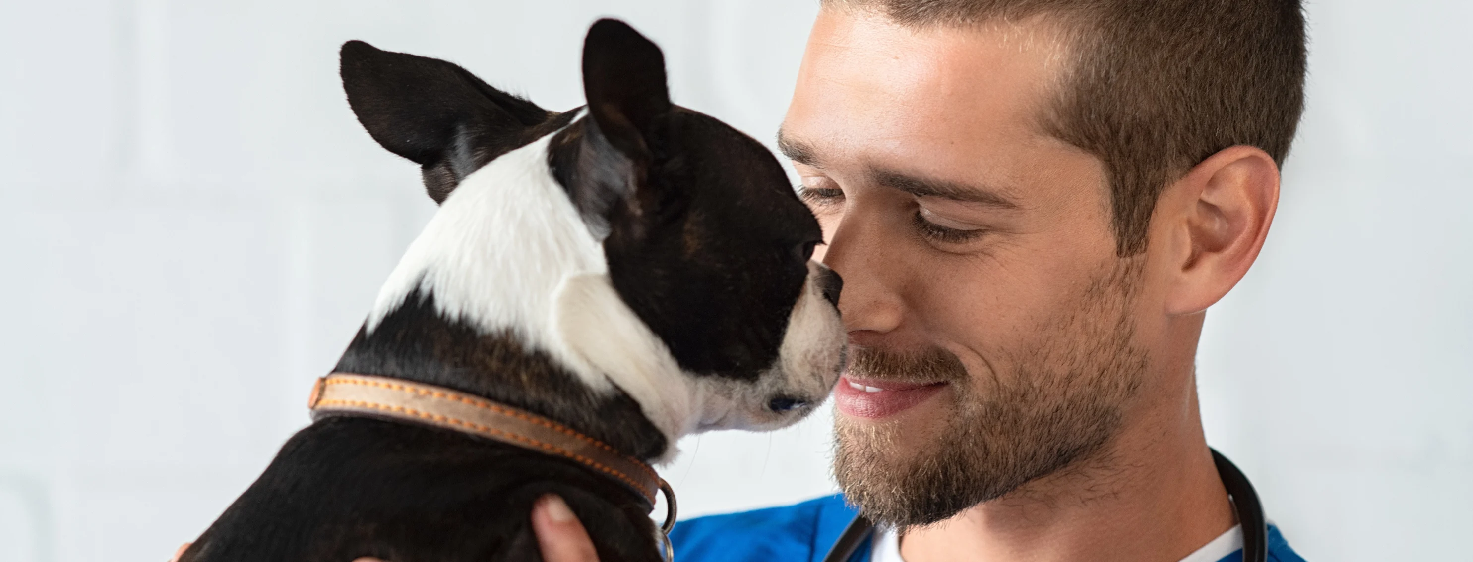 a staff member holds a black and white dog up to his nose