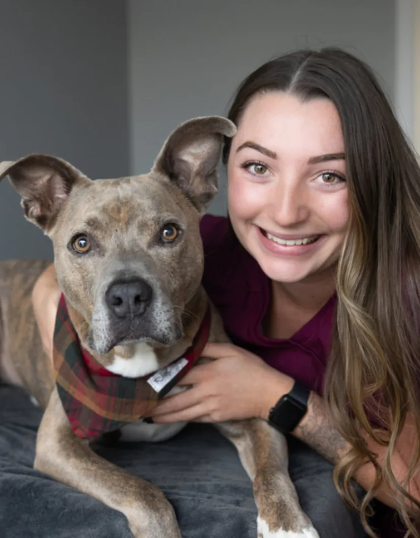 Claire smiling with a brown Pitbull with a checkered bandana on