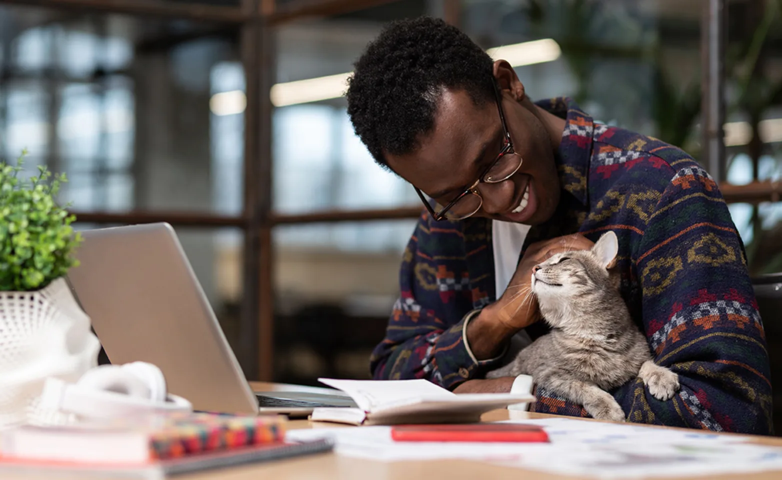 A man sitting at a desk in front of a computer holding and petting his cat. A man sitting at a desk in front of a computer holding and petting his cat.