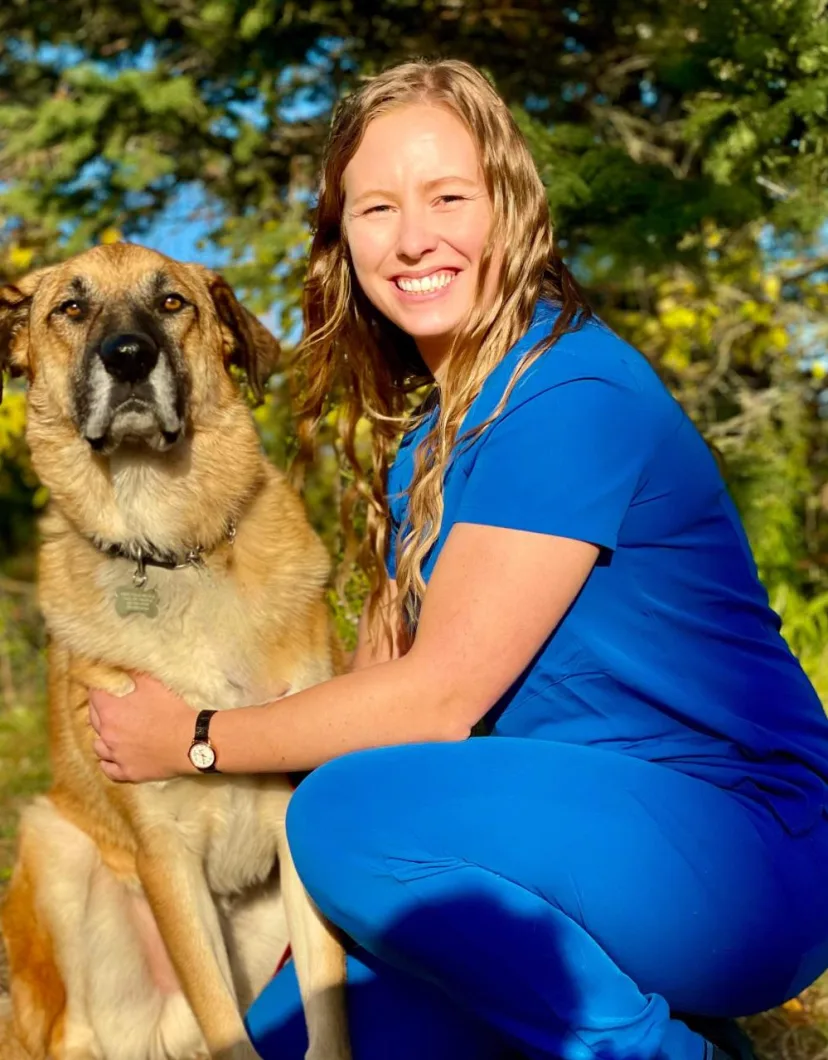 Ana in blue scrubs sitting next to a large dog.