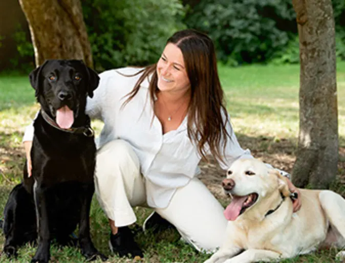 Woman kneeling with arms around two dogs outside in the grass Woman kneeling with arms around two dogs outside in the grass