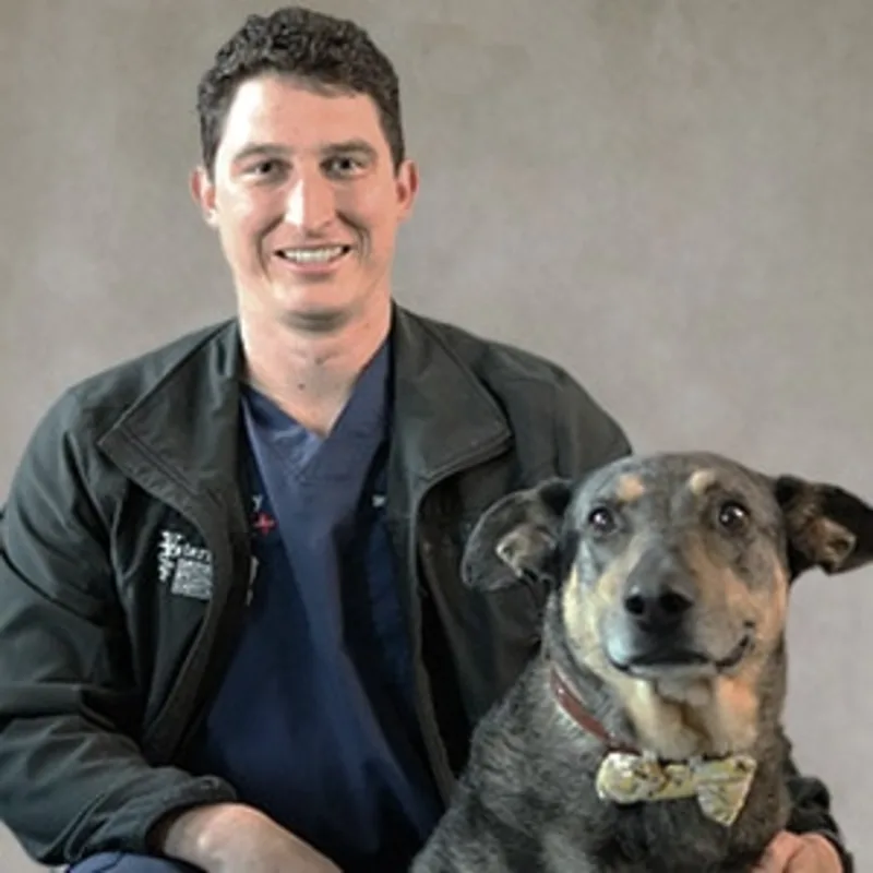 Kevin Lockman smiling in front of a grey backdrop kneeling next to a brown dog Kevin Lockman smiling in front of a grey backdrop kneeling next to a brown dog